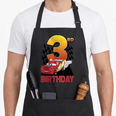 Tablier de cuisine noir avec Lightning McQueen effectuant un burn-out sous un grand chiffre 3 coloré.