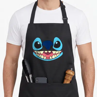 Tablier de cuisine noir avec le visage souriant de Stitch aux grands yeux bleus et dents blanches.