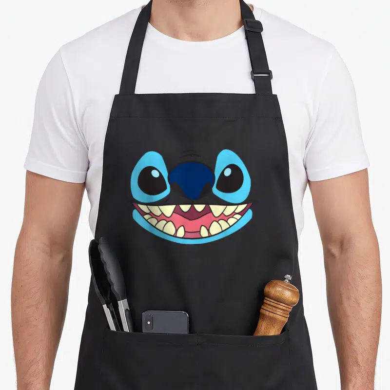 Tablier de cuisine noir avec le visage souriant de Stitch aux grands yeux bleus et dents blanches.