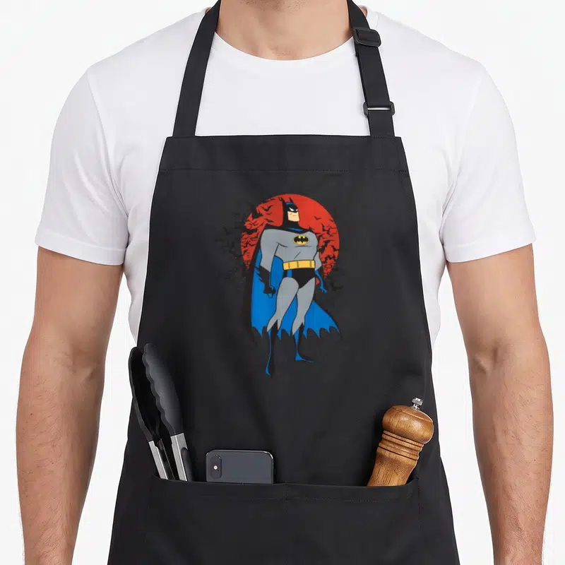 Tablier de cuisine noir avec Batman Stand Tall, cape bleue, soleil rouge et vol de chauves-souris en arrière-plan.