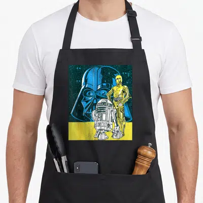 Tablier de cuisine noir avec illustration pop art de Dark Vador, C-3PO et R2-D2 sur fond étoilé bleu et bande jaune.