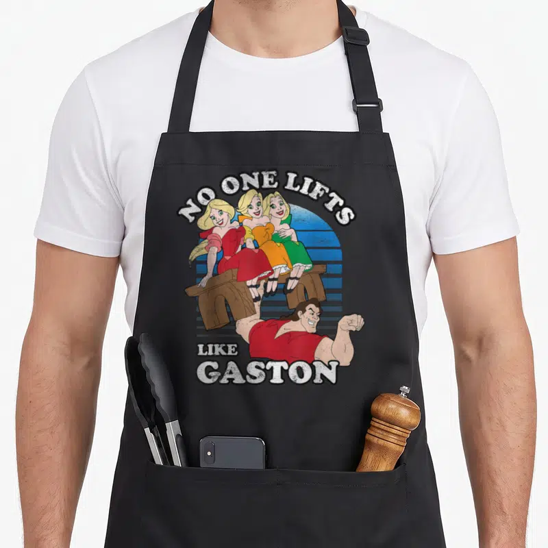 Tablier de cuisine noir avec illustration de Gaston portant un banc avec trois femmes et le texte No One Lifts Like Gaston.