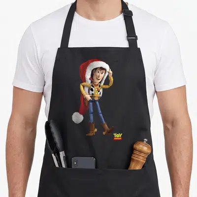 Tablier de cuisine noir avec Woody de Toy Story portant un grand chapeau de Père Noël rouge et blanc.