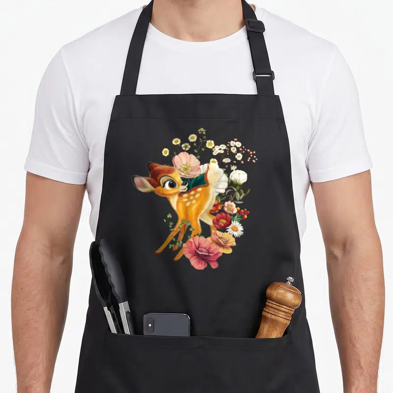 Tablier de cuisine noir avec un faon Bambi entouré de fleurs roses, blanches et jaunes.