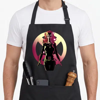 Tablier de cuisine noir avec une illustration colorée de Jean Grey en tenue noire devant un logo circulaire jaune et rose.