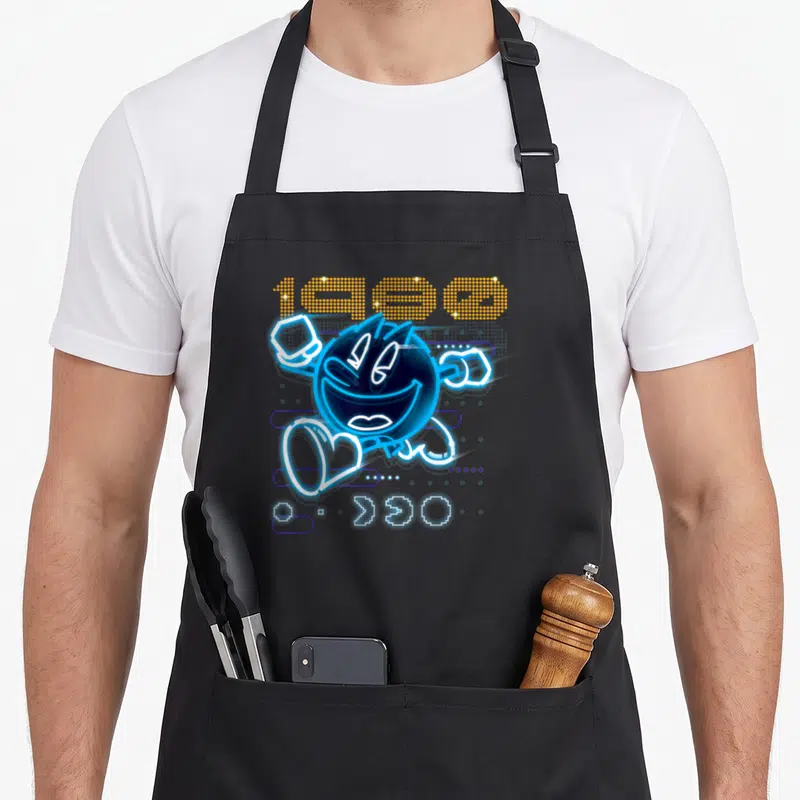 Tablier de cuisine noir avec illustration Pac-Man neon bleu et l'année 1980 en pixelisé orange.