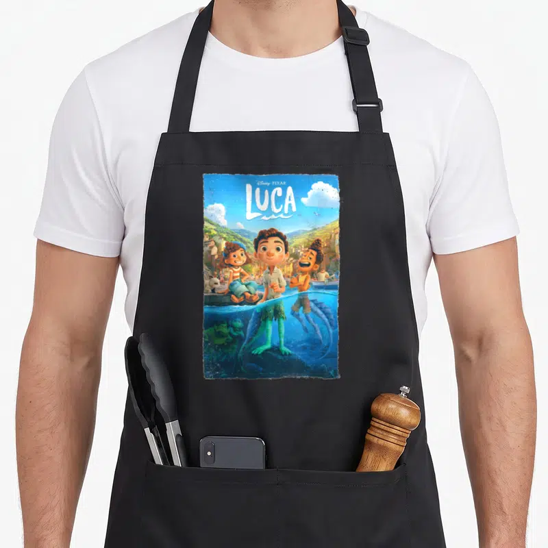 Tablier de cuisine noir avec illustration colorée de Luca et ses amis dans un style affiche de film d'animation italienne.