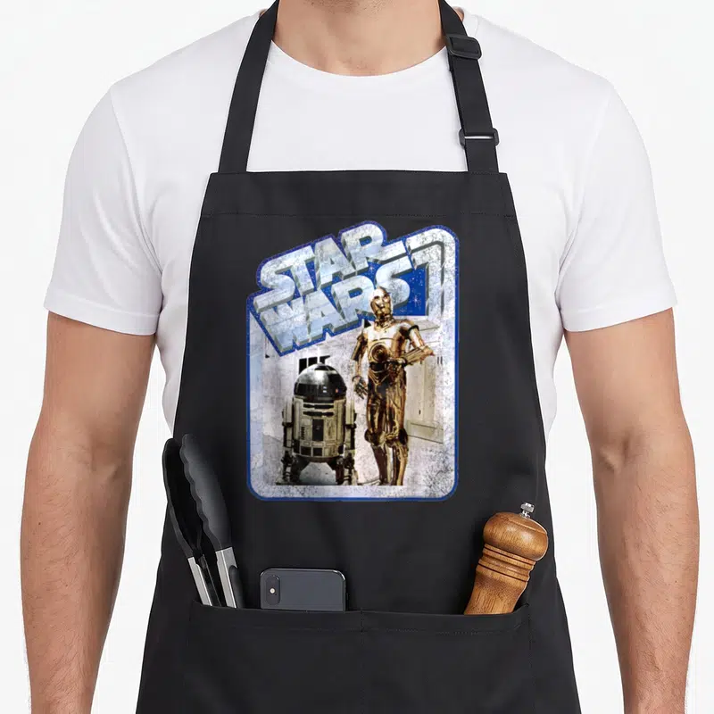 Tablier de cuisine noir avec illustration vintage de C-3PO et R2-D2 sous le logo Star Wars encadré de bleu.