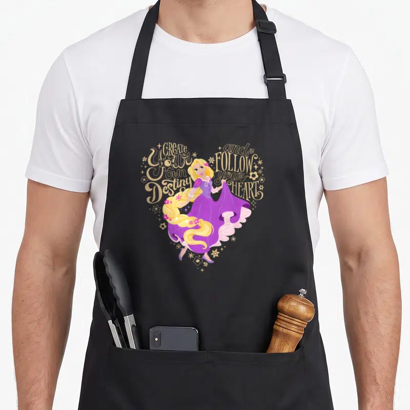 Tablier de cuisine noir avec Raiponce et texte doré formant un cœur stylisé avec des étoiles et fleurs.
