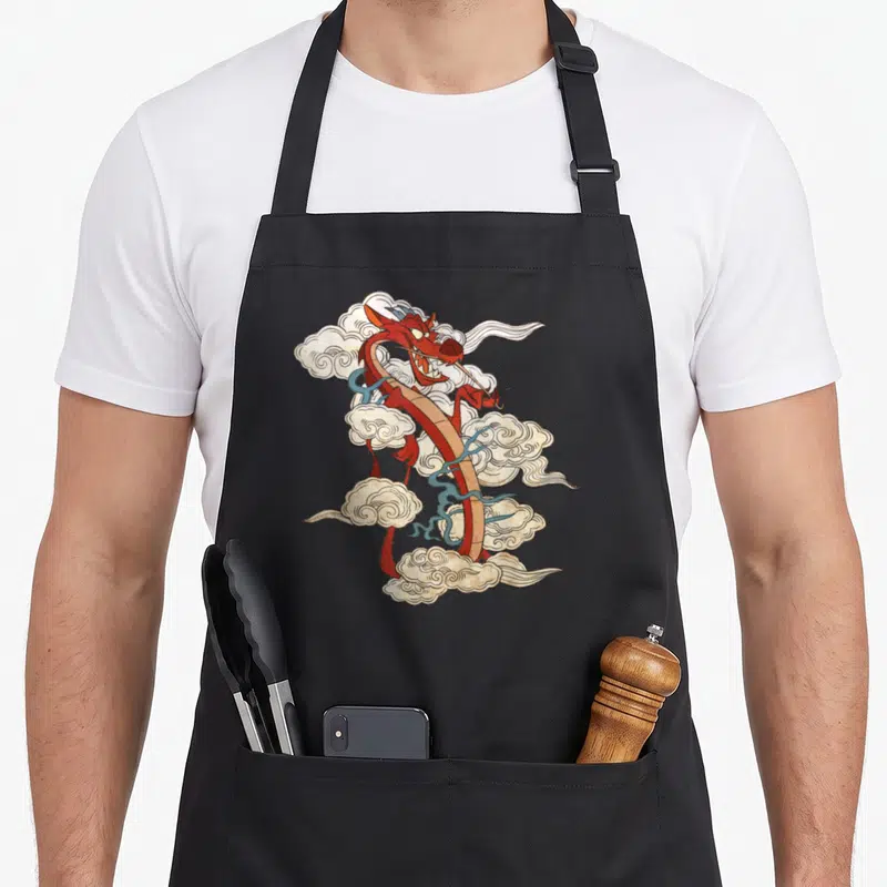 Tablier de cuisine noir avec illustration du dragon Mushu entouré de nuages stylisés dans un style graphique coloré.