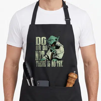 Tablier de cuisine noir avec illustration vintage de Yoda tenant sa canne et le texte Do Or Do Not There Is No Try imprimé en vert pâle.