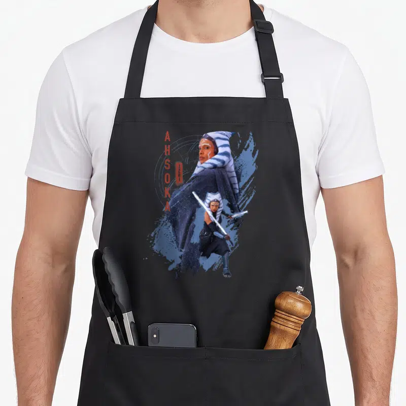 Tablier de cuisine noir avec illustration d'Ahsoka Tano Jedi Ready tenant une épée lumineuse sur fond bleu stylisé.