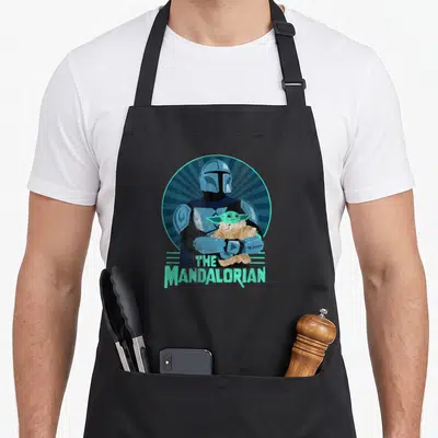 Tablier de cuisine noir avec illustration rétro du Mandalorian tenant Grogu dans un cercle bleu turquoise et le texte The Mandalorian.