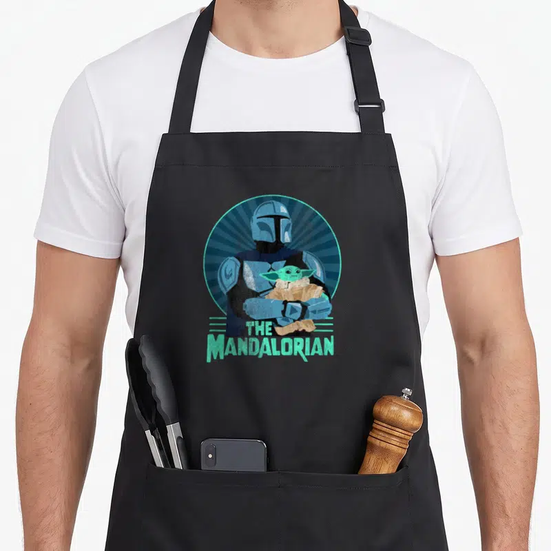 Tablier de cuisine noir avec illustration rétro du Mandalorian tenant Grogu dans un cercle bleu turquoise et le texte The Mandalorian.