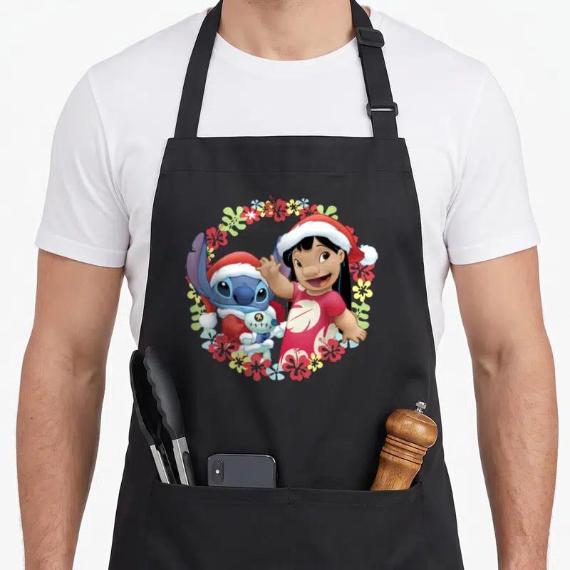 Tablier de cuisine noir avec Lilo et Stitch en bonnets rouges entourés de fleurs tropicales colorées.