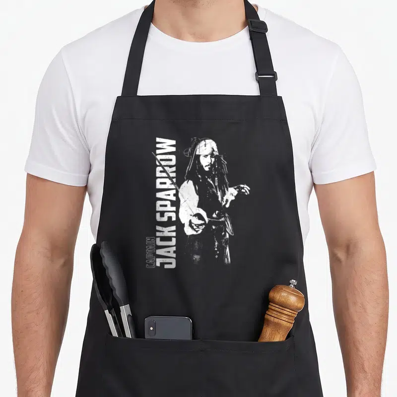 Tablier de cuisine noir avec illustration blanche de Captain Jack Sparrow tenant un sabre et son nom imprimé verticalement.