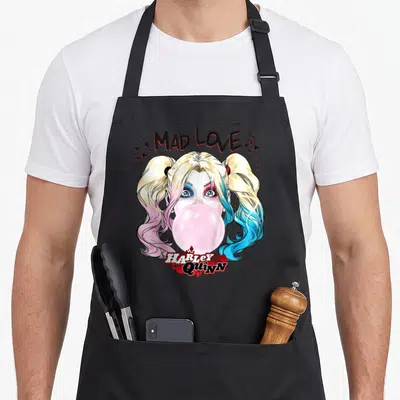 Tablier de cuisine noir avec illustration Harley Quinn aux cheveux roses et bleus crachant une bulle de gum rose.