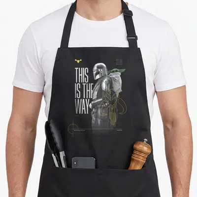 Tablier de cuisine noir avec illustration du Mandalorian, Grogu et le texte This Is The Way en typographie verticale.