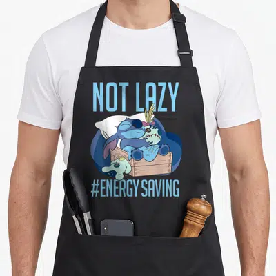 Tablier de cuisine noir avec Stitch dormant sur une caisse et le texte Not Lazy Energy Saving en bleu clair.