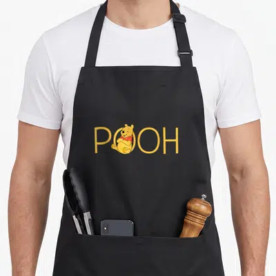 Tablier de cuisine noir avec illustration de Winnie l'ourson assis dans le mot POOH en lettres jaunes.