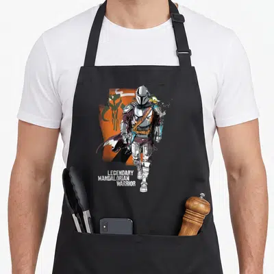 Tablier de cuisine noir avec illustration du Mandalorian, Grogu et texte Legendary Warrior sur fond orange.