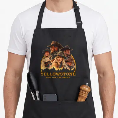 Tablier de cuisine noir avec illustration group shot de personnages en chapeaux cowboy et texte Yellowstone Ride For The Brand.