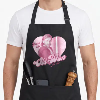 Tablier de cuisine noir avec portrait d'Obi-Wan Kenobi dans un cœur rose et texte You're the Obi-Wan for me en lettres stylisées.