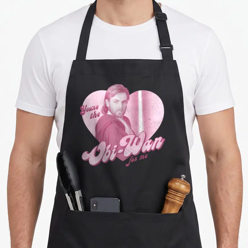 Tablier de cuisine noir avec portrait d'Obi-Wan Kenobi dans un cœur rose et texte You're the Obi-Wan for me en lettres stylisées.