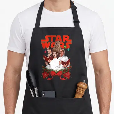 Tablier de cuisine noir avec Han Solo, Leia, Luke et Chewbacca en chœur de Noël sous le logo Star Wars.