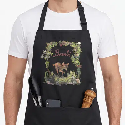 Tablier de cuisine noir avec un portrait de Bambi encadré de fleurs, de feuilles et d'amis animaux dans un style vintage doux.