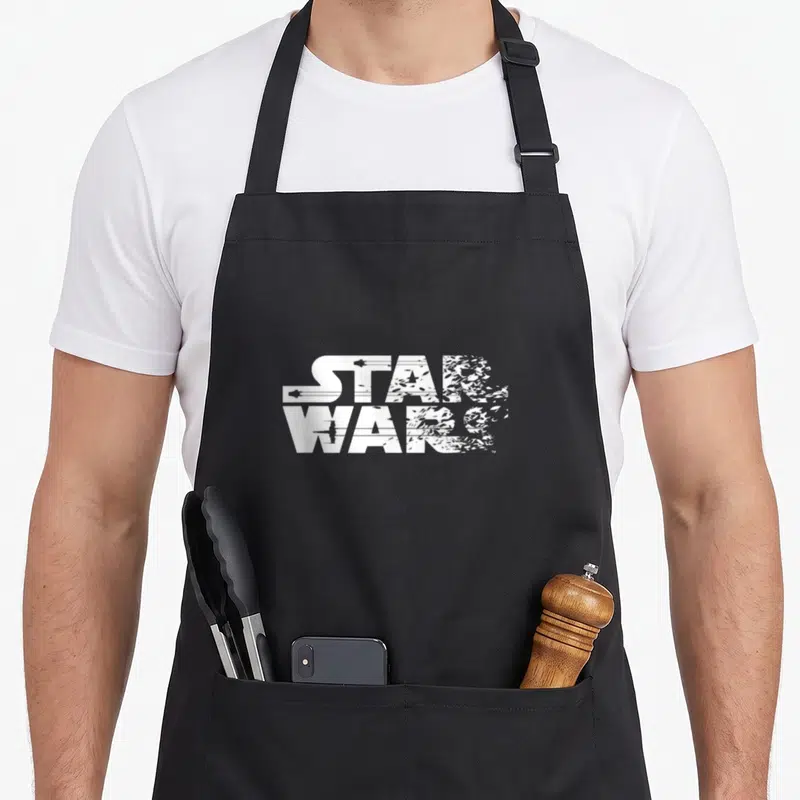 Tablier de cuisine noir avec le logo Star Wars en blanc, style fragmenté et érodé au centre du torse.
