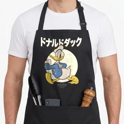 Tablier de cuisine noir avec illustration de Donald Duck en pose dynamique sous des caractères japonais blancs sur fond circulaire crème.