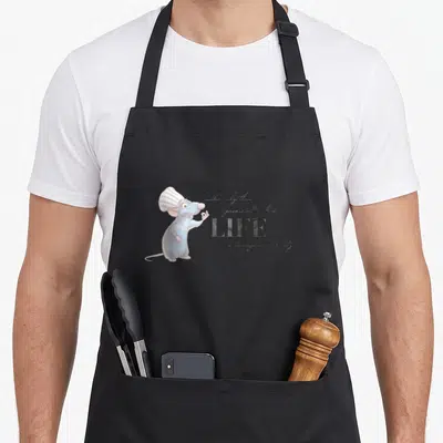 Tablier de cuisine noir avec Remy en toque blanche et texte calligraphié sur fond gris uni.