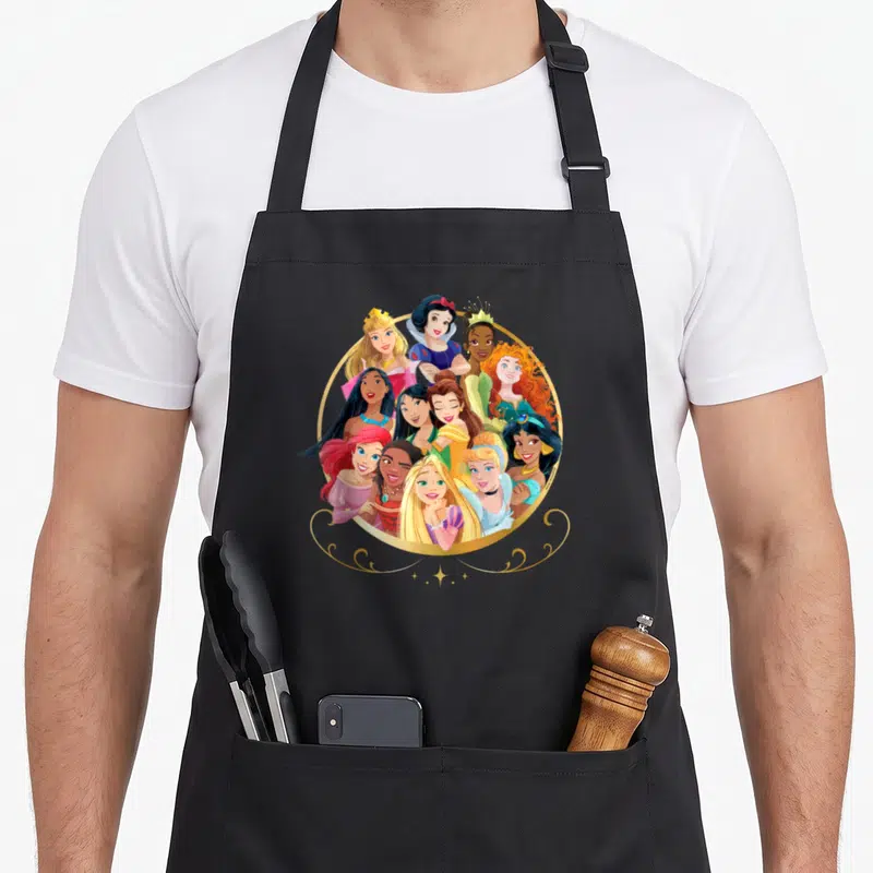 Tablier de cuisine noir avec un groupe de princesses souriantes dans un cadre doré circulaire.