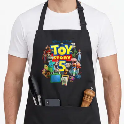 Tablier de cuisine noir avec le logo Toy Story 5 et des personnages colorés comme Buzz, Woody et Forky imprimés au centre.