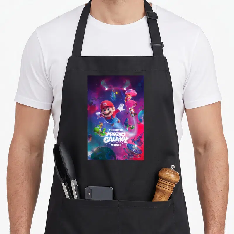 Tablier de cuisine noir avec une illustration de Mario, Yoshi et la Princesse Peach dans un décor spatial coloré.