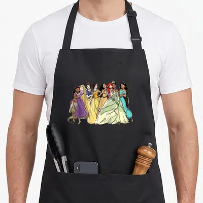 Tablier de cuisine noir avec illustration de sept princesses Disney dessinées au crayon coloré se tenant par la main.