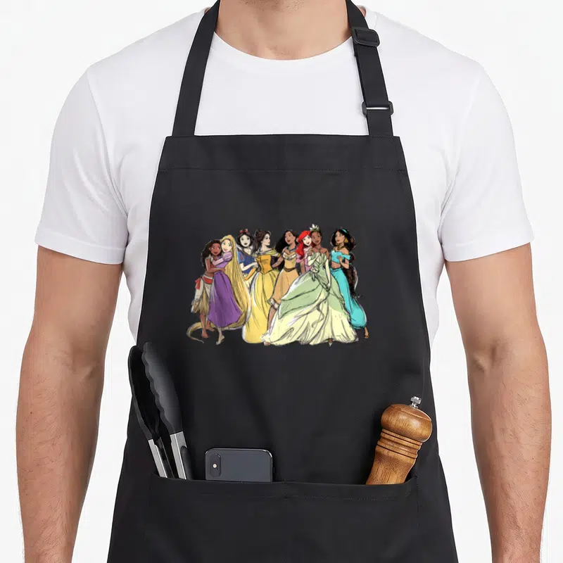 Tablier de cuisine noir avec illustration de sept princesses Disney dessinées au crayon coloré se tenant par la main.