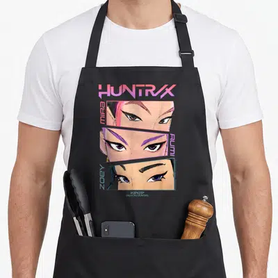 Tablier de cuisine noir avec illustration des yeux de Mira, Rumi et Zoey du titre Huntrix en lettres roses et violettes.