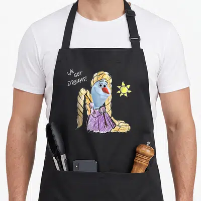 Tablier de cuisine noir avec Olaf déguisé en Raiponce et l'inscription We Got Dreams à côté d'un soleil jaune.