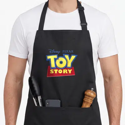 Tablier de cuisine noir avec le logo coloré Toy Story de Disney Pixar en lettres jaunes et bleues sur fond rouge.