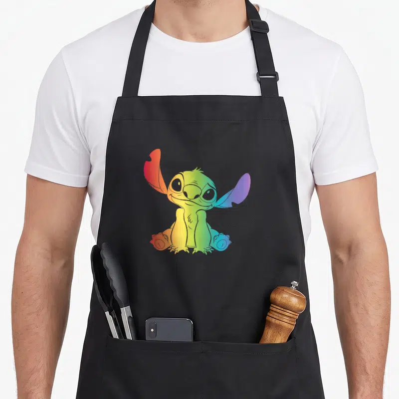 Tablier de cuisine noir avec Stitch arc-en-ciel assis entouré de Lilo et d'aliens colorés.