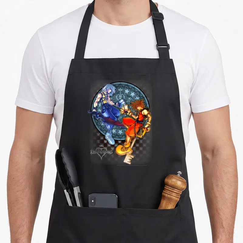 Tablier de cuisine noir avec Sora et Riku brandissant leurs Keyblades devant un motif circulaire.