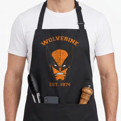 Tablier de cuisine noir avec le visage stylisé de Wolverine en orange et le texte Est. 1974 imprimé au centre.