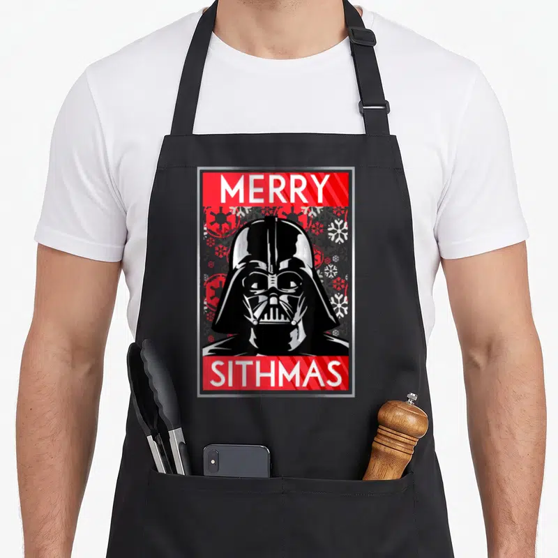 Tablier de cuisine noir avec illustration de Darth Vader et texte Merry Sithmas sur fond de motifs de neige.