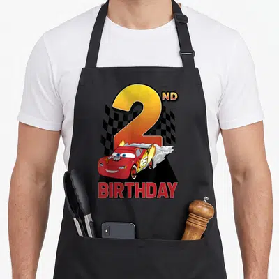 Tablier de cuisine noir avec Lightning McQueen effectuant un dérapage sous un grand chiffre 2 et l'inscription anniversaire.