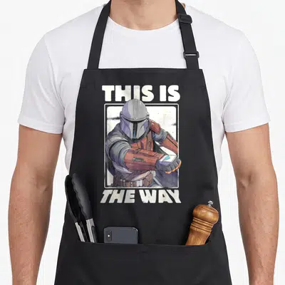 Tablier de cuisine noir avec portrait du Mandalorian et texte This Is The Way en blanc.