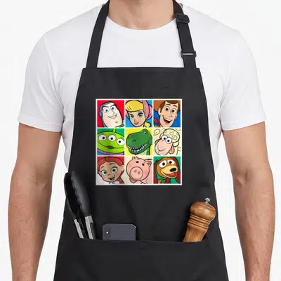 Tablier de cuisine noir avec une grille de neuf portraits colorés des personnages de Toy Story incluant Buzz, Woody et Rex.