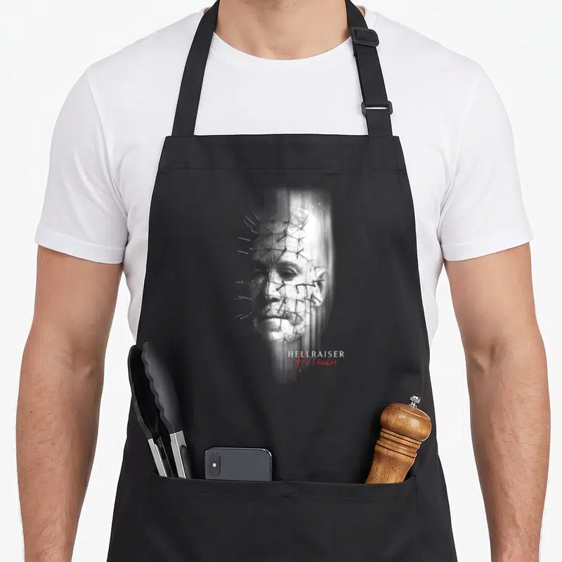 Tablier de cuisine noir avec le visage de Pinhead et les mots HEULRAISER Hellseeker imprimés en blanc et rouge.
