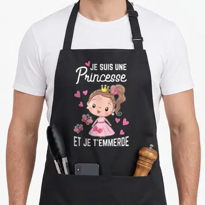 Tablier de cuisine noir avec une princesse rose, des cœurs et le texte Je suis une Princesse et je t'emmerte imprimé en blanc.